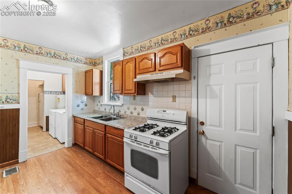Image 18 of 27: Kitchen featuring white gas stove, brown cabinetry, light countertops, ligh
