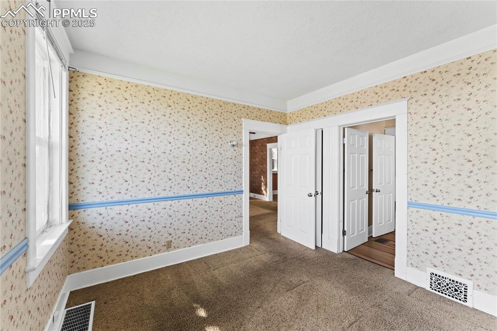 Image 7 of 27: Spare room with wallpapered walls, carpet floors, and a textured ceiling