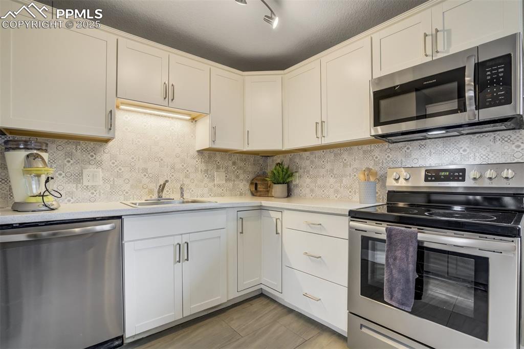 Image 10 of 29: Kitchen featuring stainless steel appliances, decorative backsplash, white