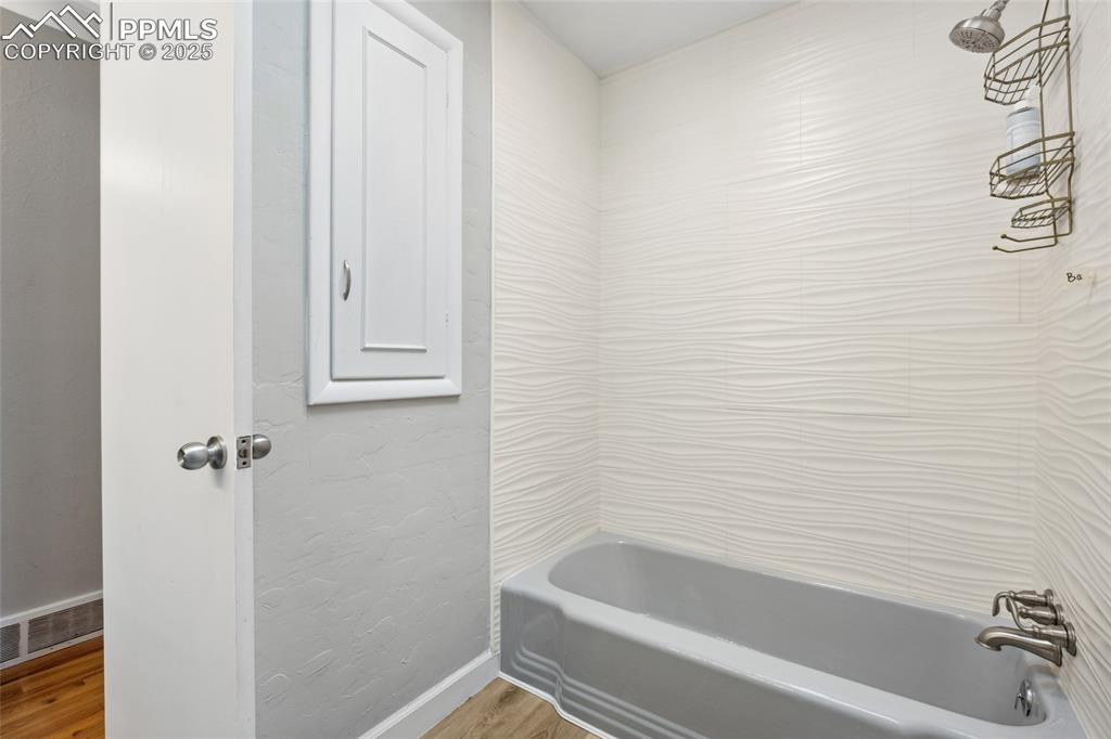 Image 22 of 39: Full bath featuring visible vents, shower combination, wood finished floor