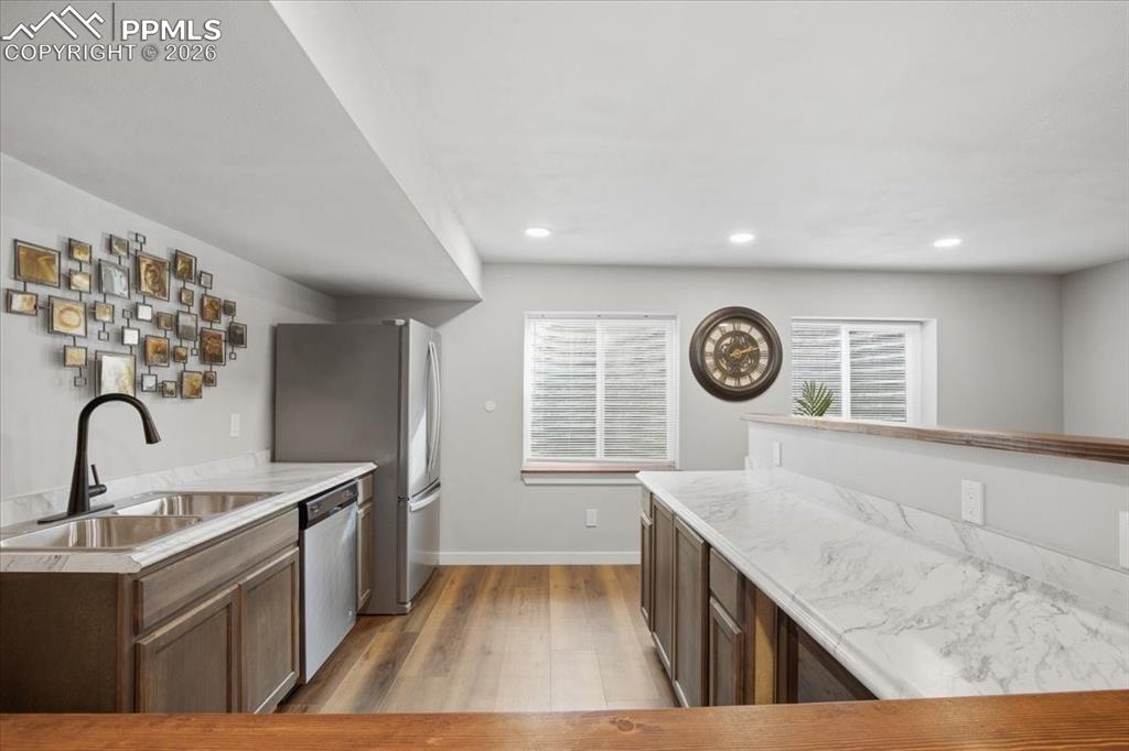 Image 32 of 40: wetbar featuring brown cabinetry, light wood finished floors, and stainless
