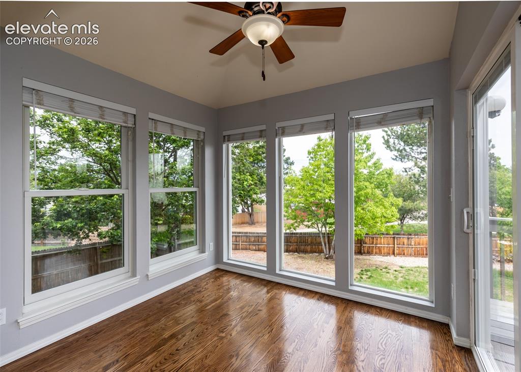 Image 21 of 41: Sunlit room with wood-finish flooring, vaulted ceiling, and a ceiling fan