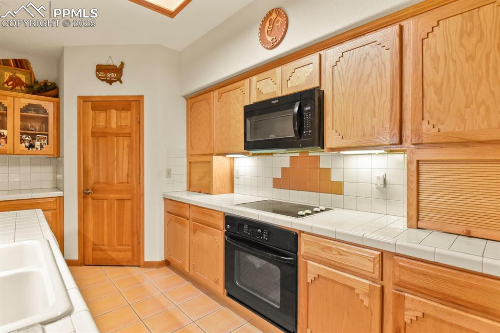 Image 11 of 48: Kitchen featuring tasteful backsplash, black appliances, light tile pattern