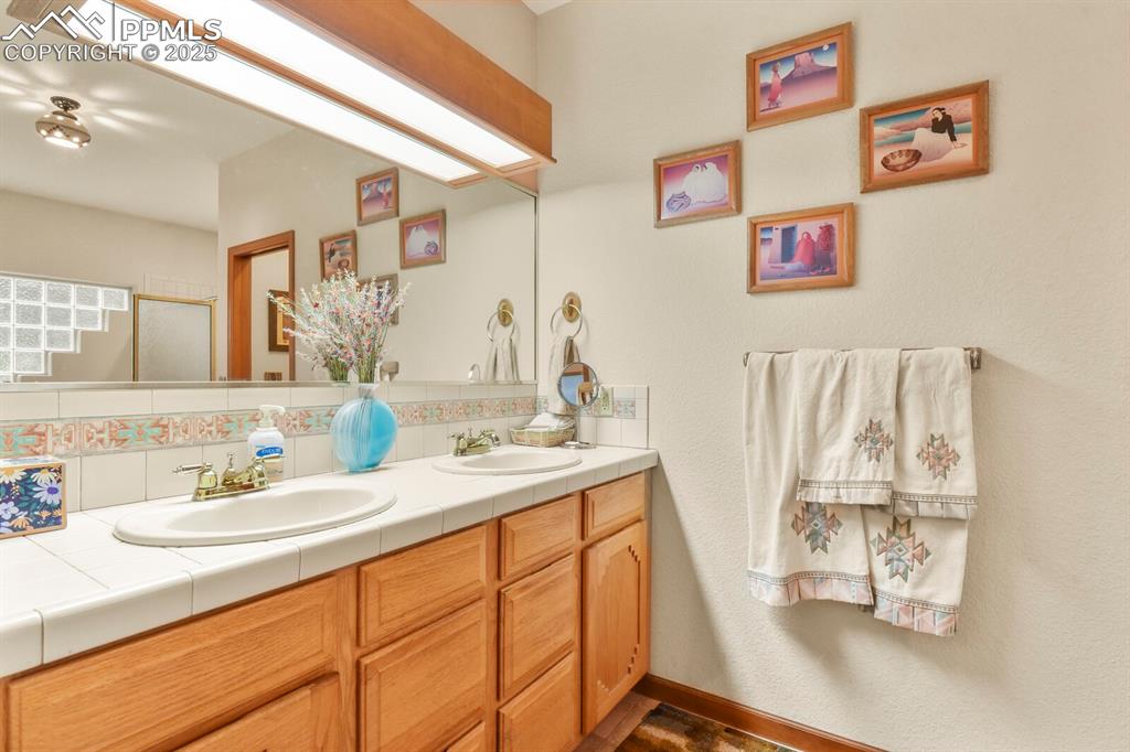 Image 20 of 48: Full bathroom with double vanity, a stall shower, and backsplash