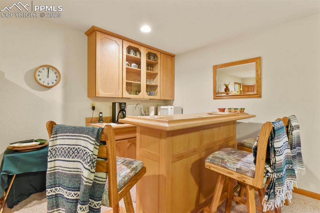Image 28 of 48: Indoor wet bar featuring light brown cabinetry, light countertops, glass in