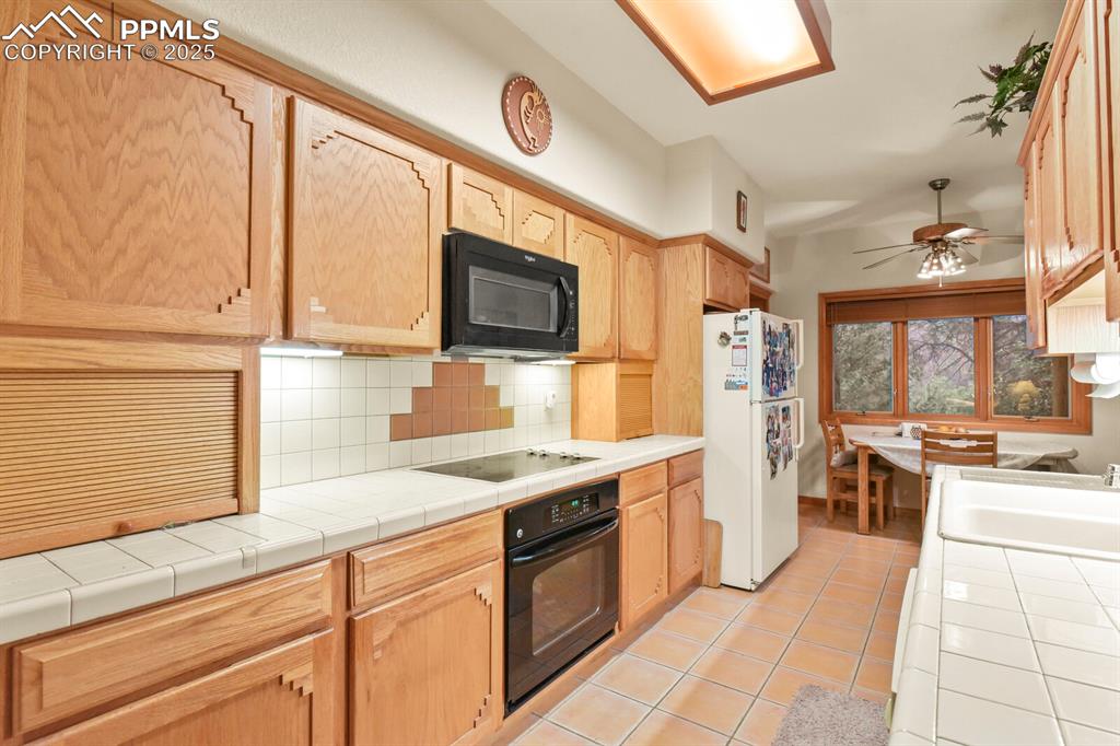 Image 9 of 48: Kitchen with tile counters, decorative backsplash, black appliances, light