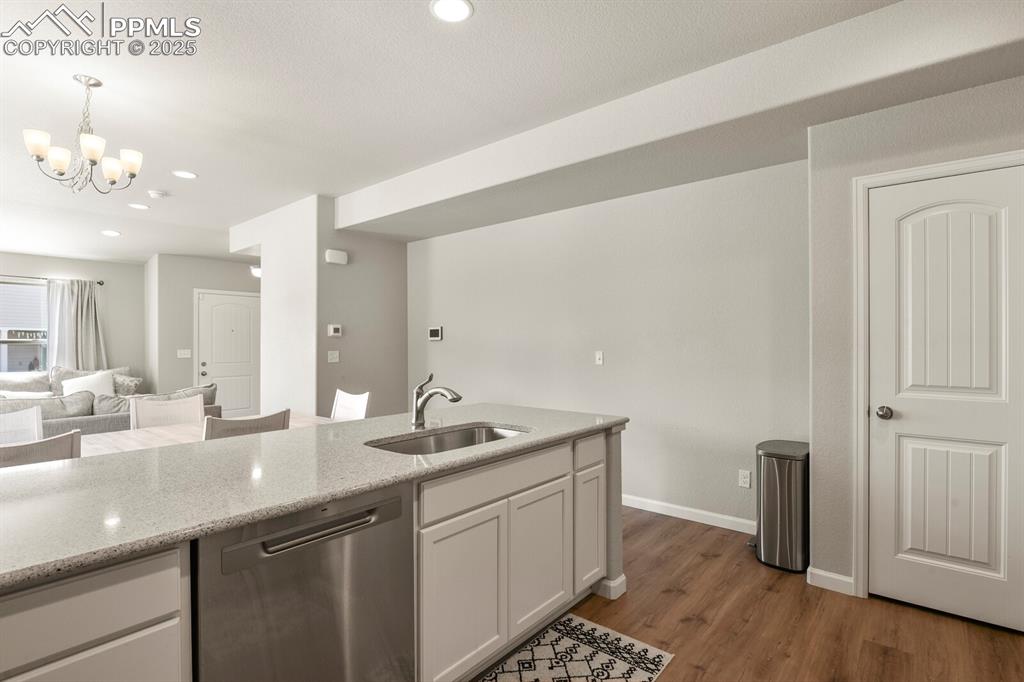 Image 10 of 27: Kitchen with dishwasher, white cabinets, light stone counters, dark wood-ty