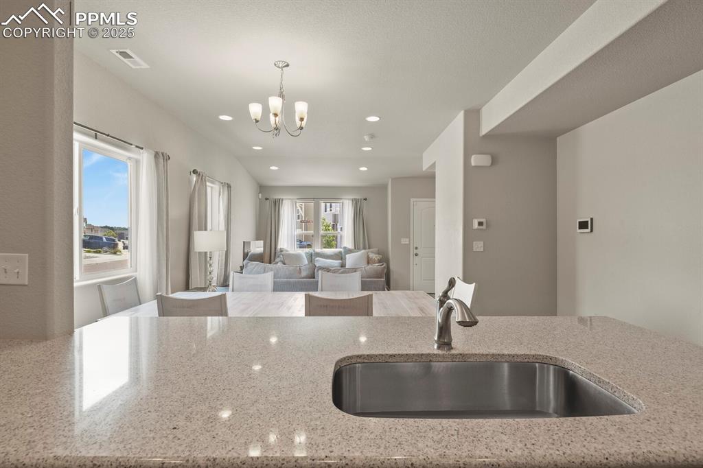 Image 11 of 27: Kitchen featuring light stone counters, a chandelier, hanging light fixture