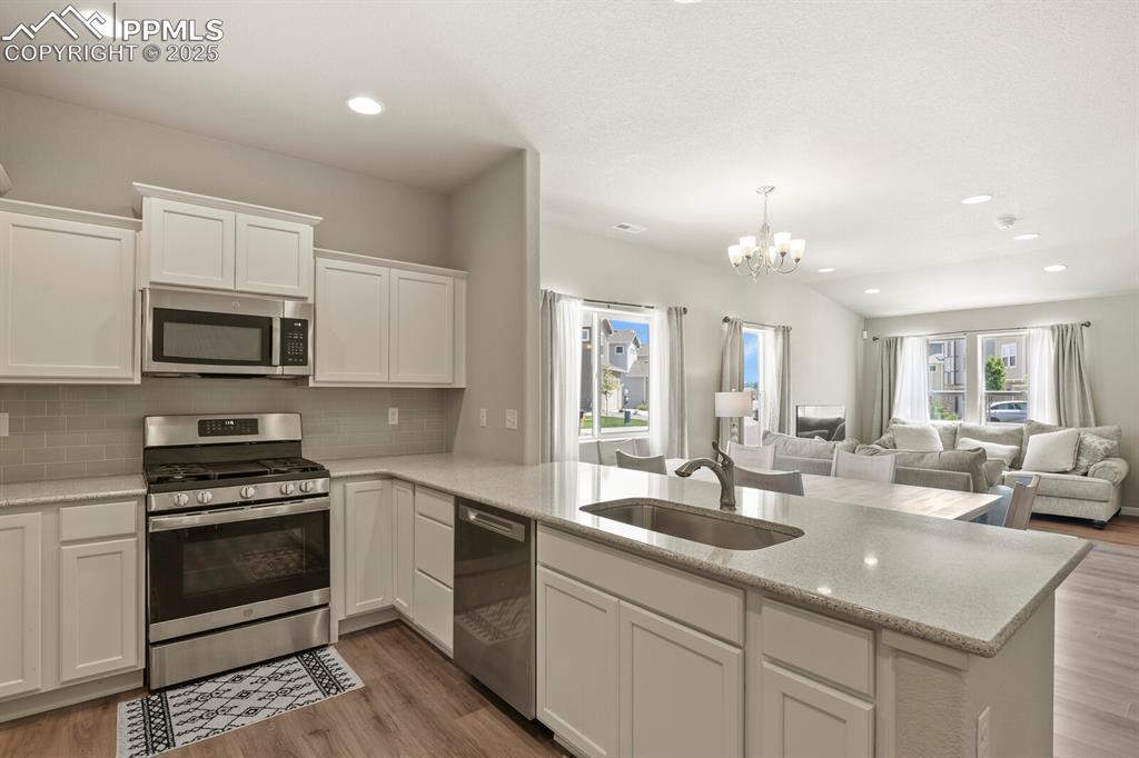 Image 9 of 27: Kitchen with stainless steel appliances, white cabinets, a chandelier, tast