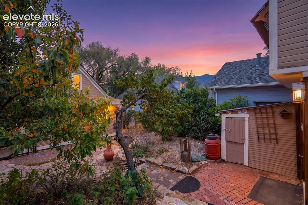 Image 34 of 40: Brick patio with an exterior storage shed and mature landscaping, featuring