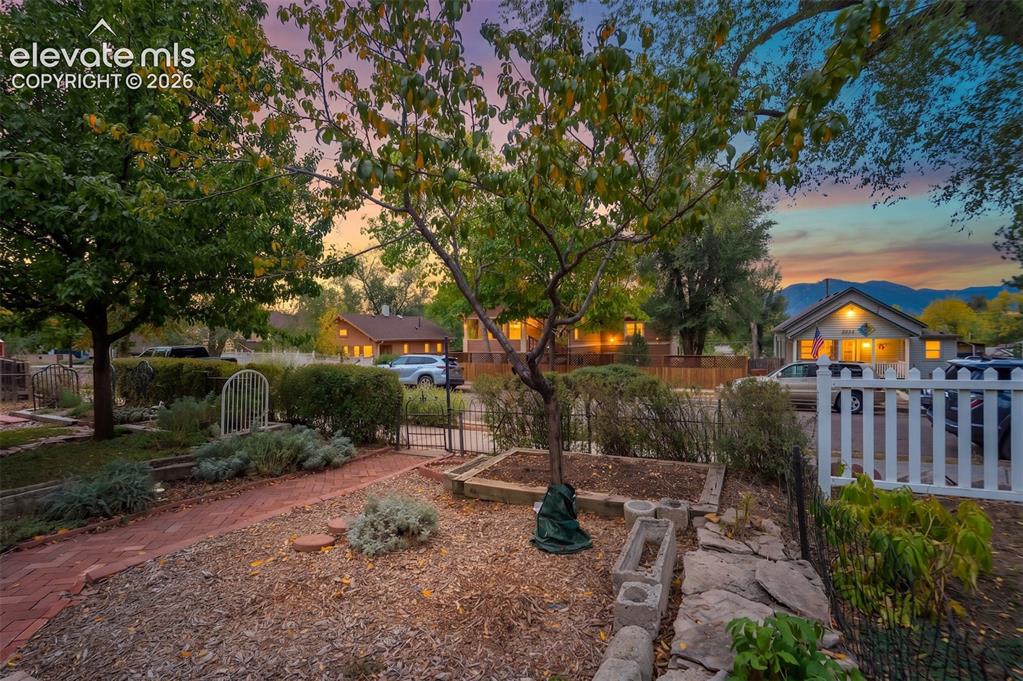 Image 35 of 40: Brick pathway, raised garden beds, white picket fence, mature trees, mounta