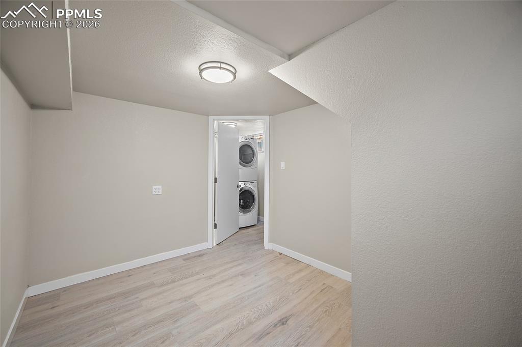 Image 21 of 29: Laundry room featuring stacked washer and dryer, light wood finished floors