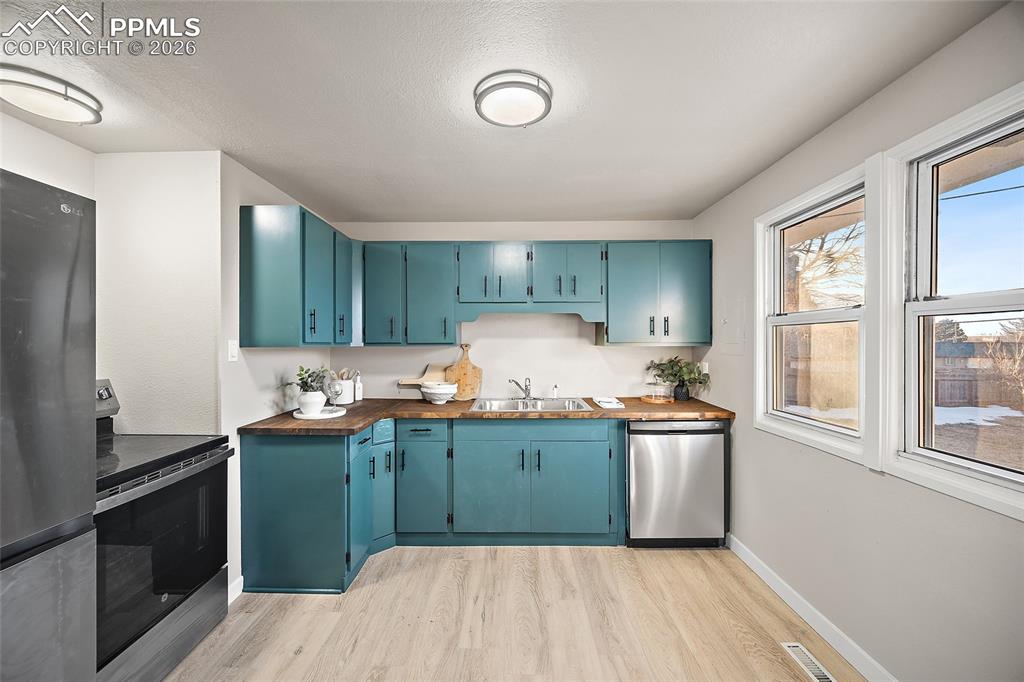 Image 7 of 29: Kitchen featuring stainless steel appliances, wooden counters, blue cabinet