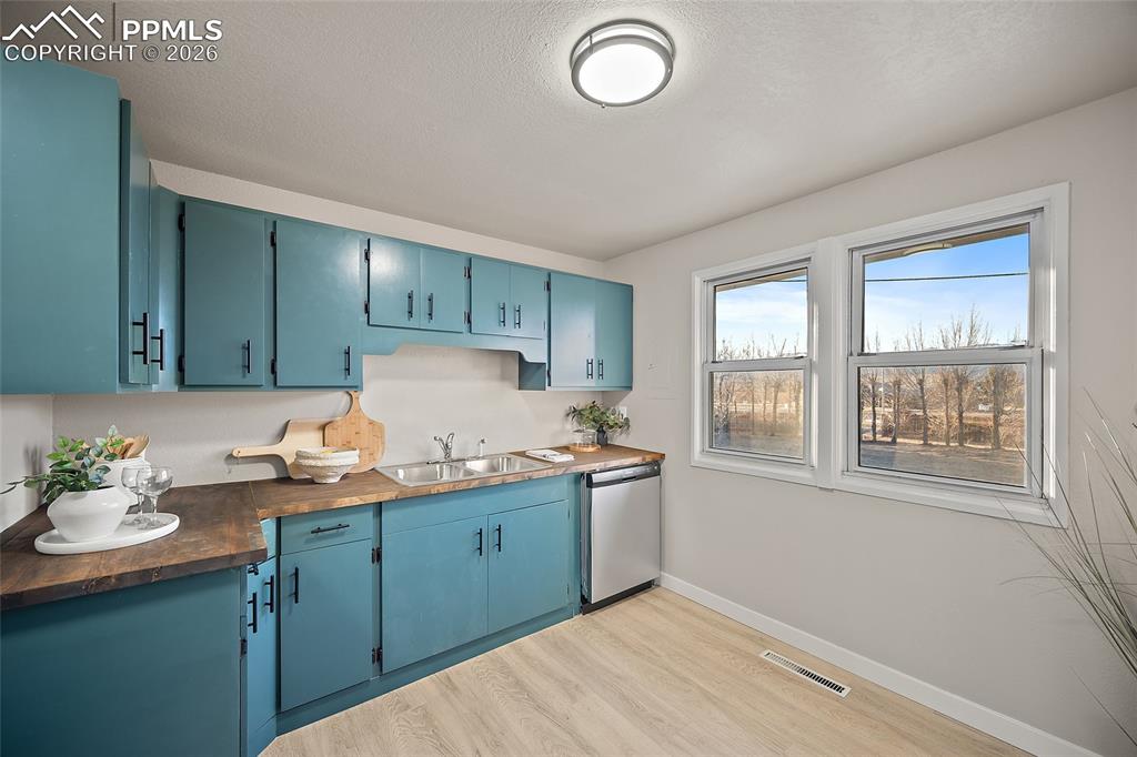 Image 8 of 29: Kitchen with blue cabinets, light wood finished floors, dishwasher, wood co