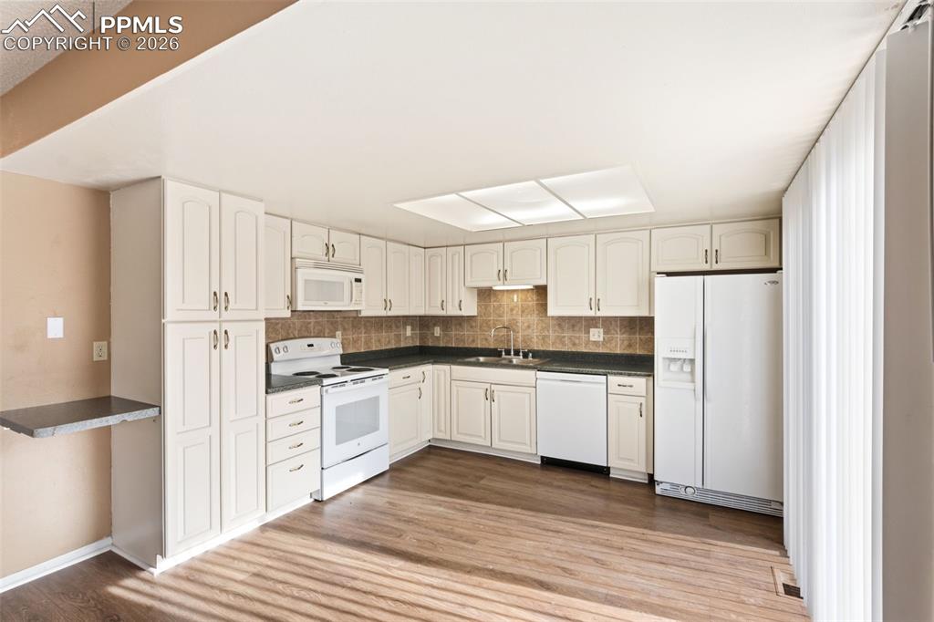 Image 16 of 47: Kitchen featuring white appliances, dark countertops, decorative backsplash