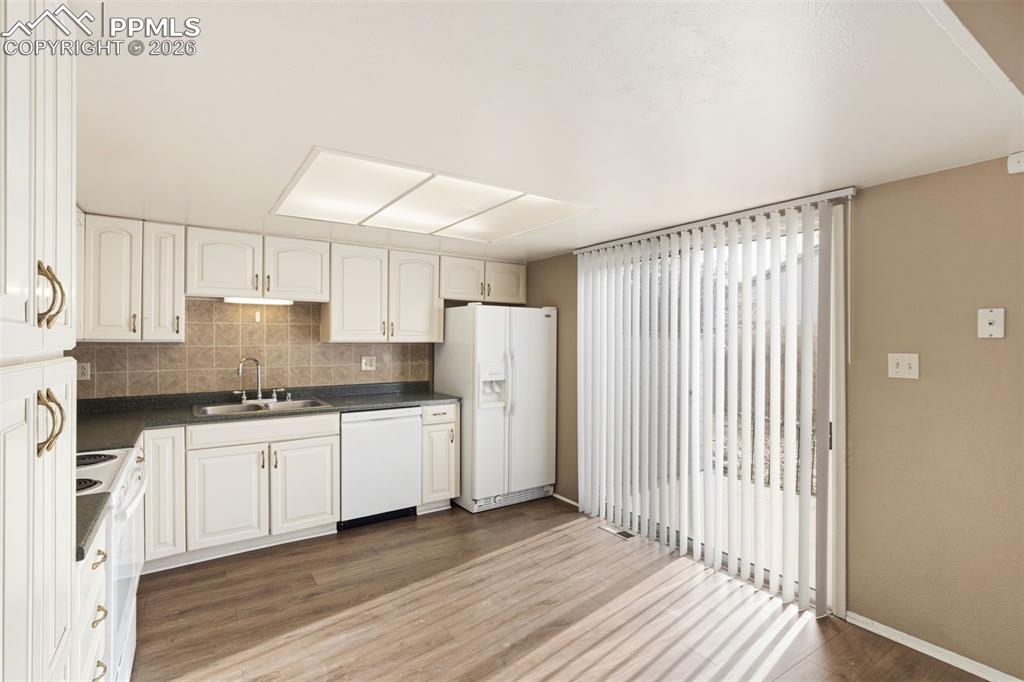 Image 17 of 47: Kitchen featuring white appliances, dark countertops, wood-type flooring, a