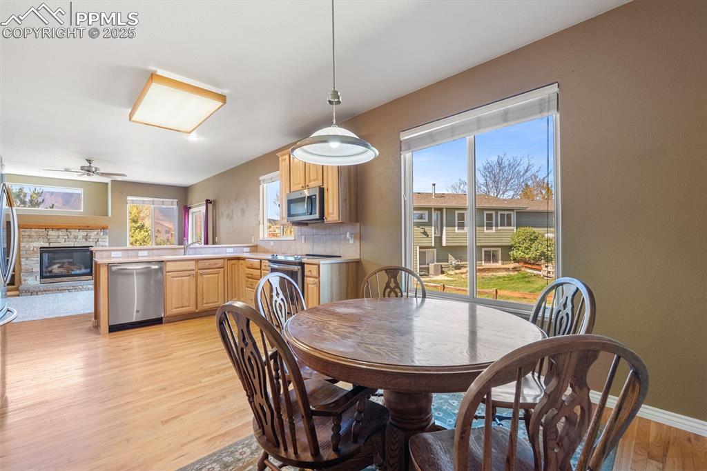 Image 6 of 50: Dining area featuring a fireplace, light wood-type flooring, and ceiling fa