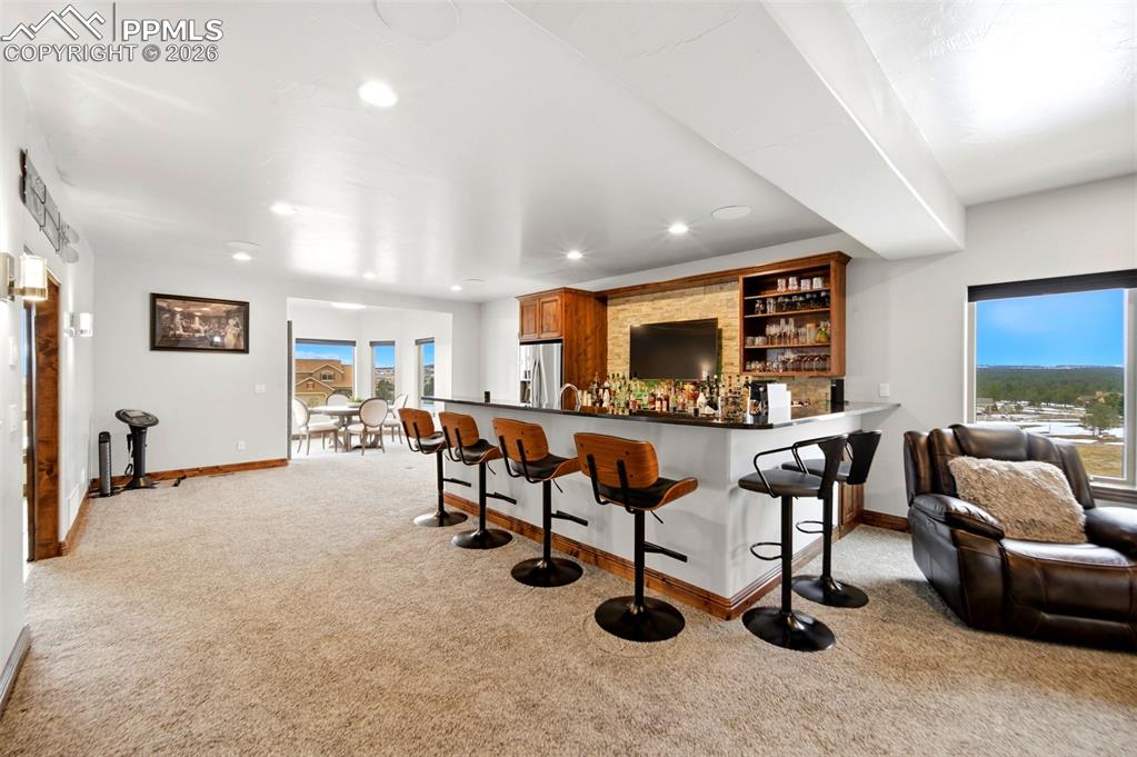 Image 14 of 48: Indoor bar with dark countertops, open shelves, light carpet, stainless ste