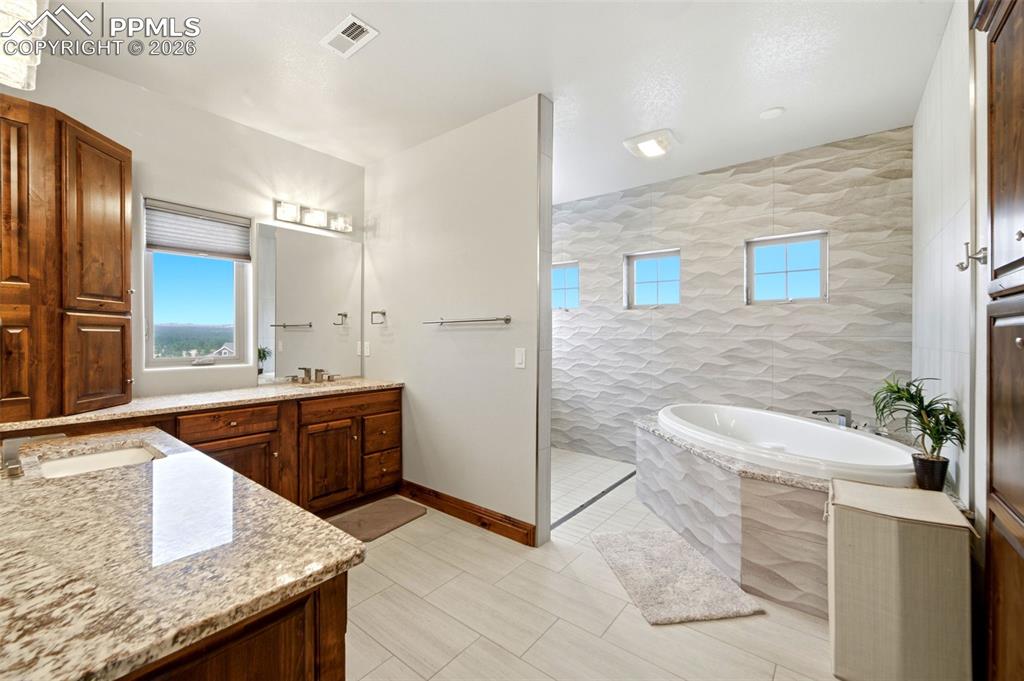 Image 21 of 48: Bathroom featuring vanity, a walk in shower, a bath, tile walls, and light