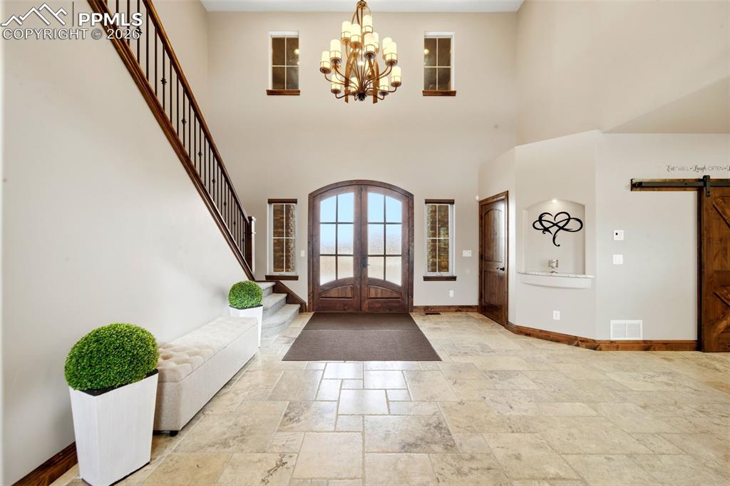 Image 7 of 48: Foyer entrance with a barn door, stone tile floors, suspended lighting, fre