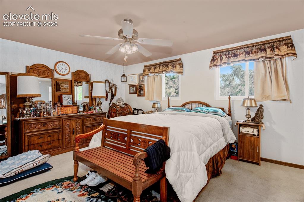 Image 16 of 45: Spacious primary bedroom featuring rich wood furnishings, ceiling fan with 