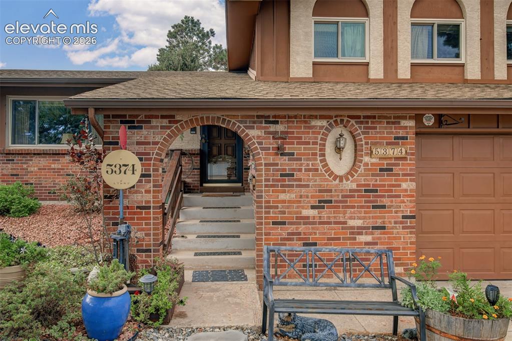 Image 29 of 45: Brick exterior with an arched entry, concrete steps, and an integrated gara
