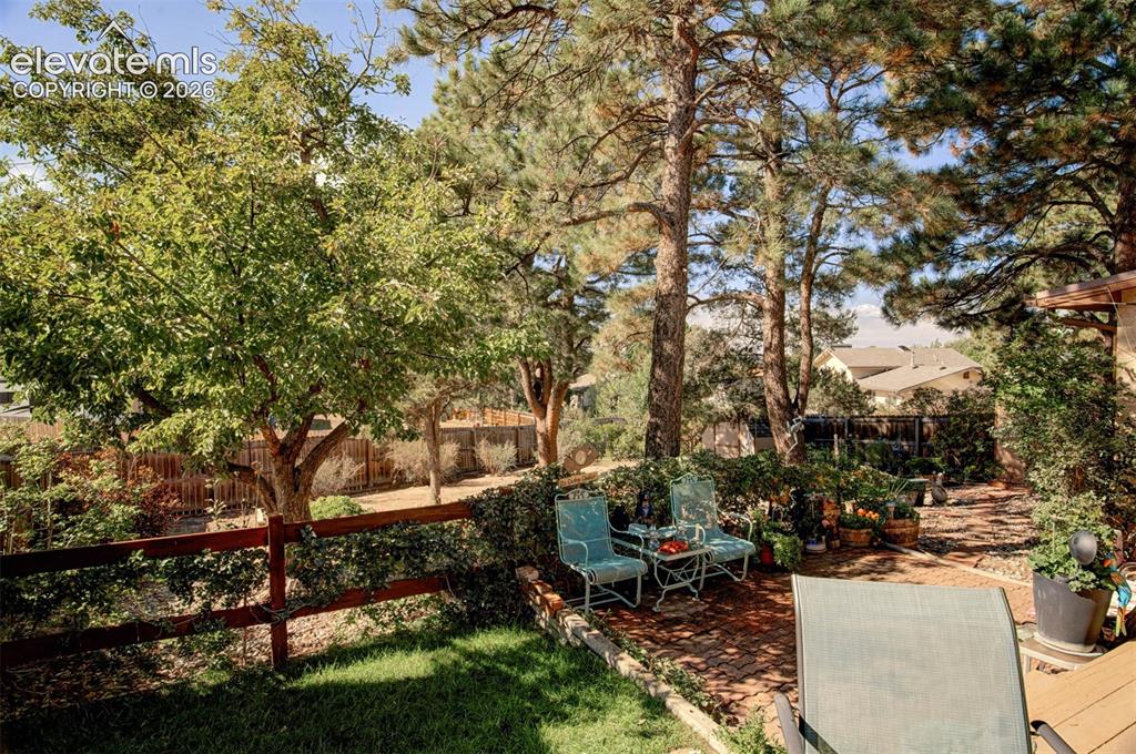 Image 34 of 45: Terraced backyard with mature trees, a brick paver patio, wood fencing, and