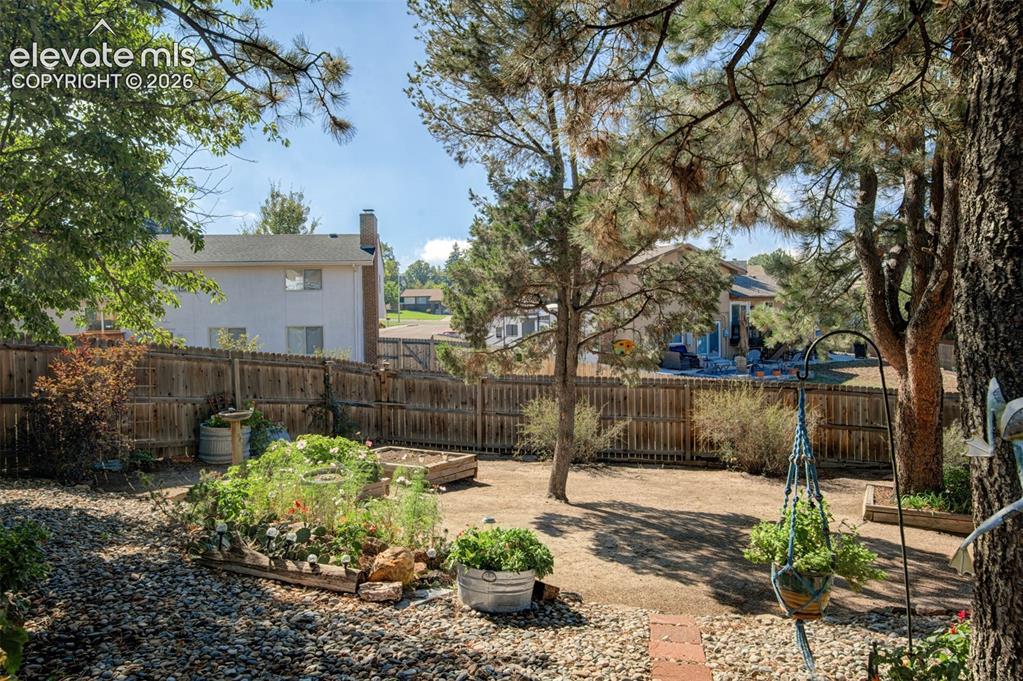 Image 35 of 45: Expansive backyard featuring mature trees, raised garden beds, a fenced per