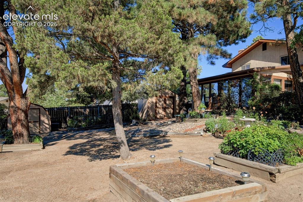 Image 36 of 45: Expansive backyard featuring mature trees, raised planter beds, a storage s
