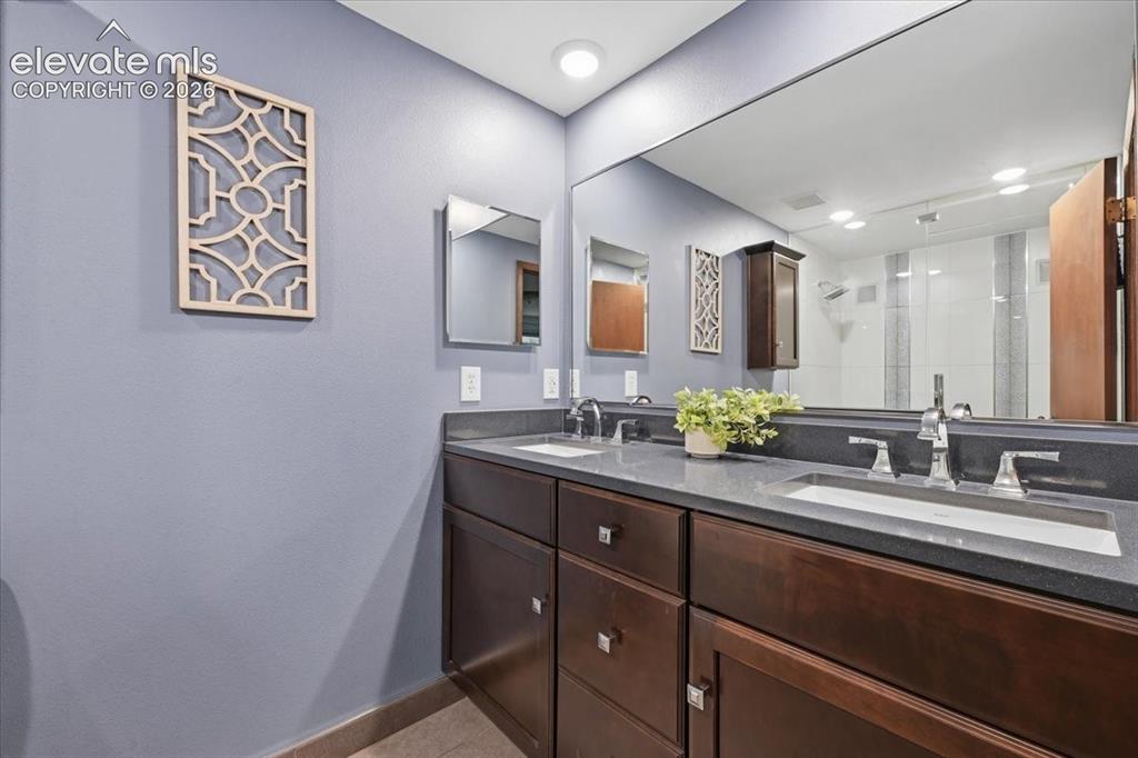 Image 27 of 50: Dual vanity with dark wood-finish cabinetry, integrated sinks, and polished