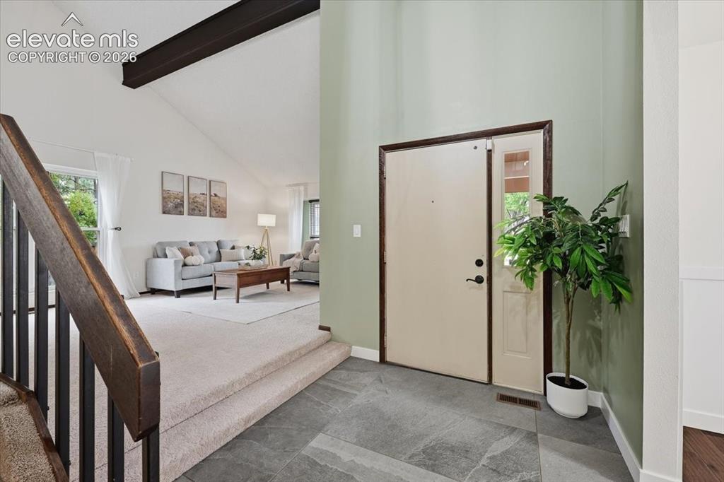 Image 7 of 50: Tiled entryway leading to a living area with vaulted ceilings and exposed b