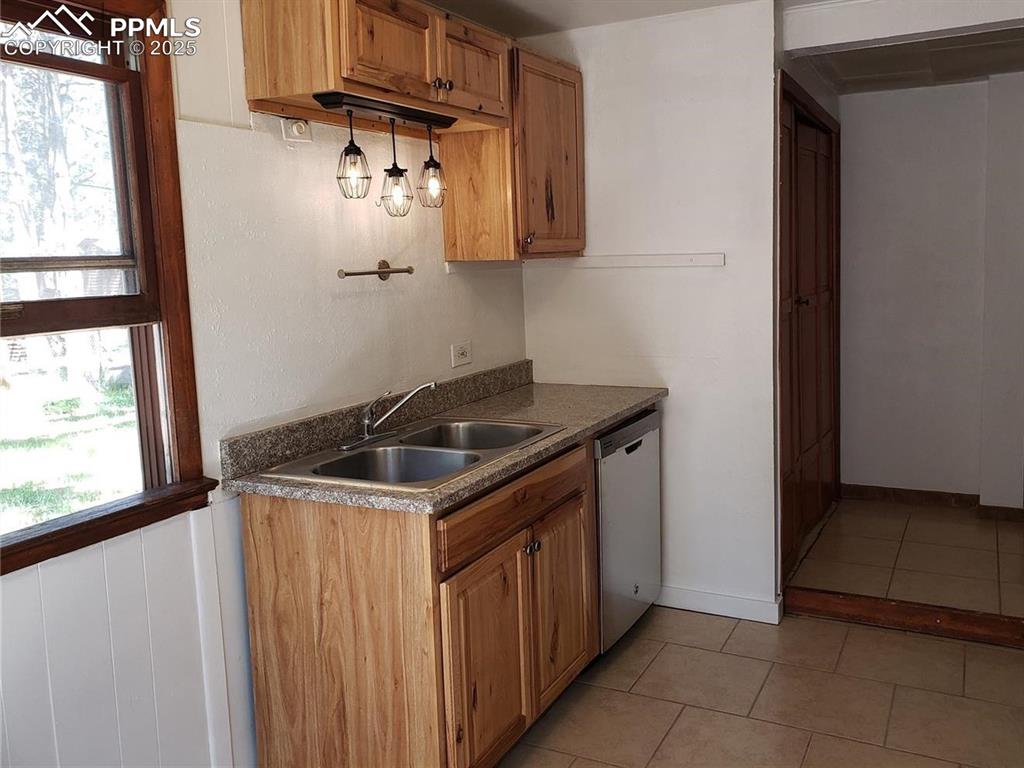 Image 10 of 20: Kitchen with light tile patterned floors, dark countertops, brown cabinetry