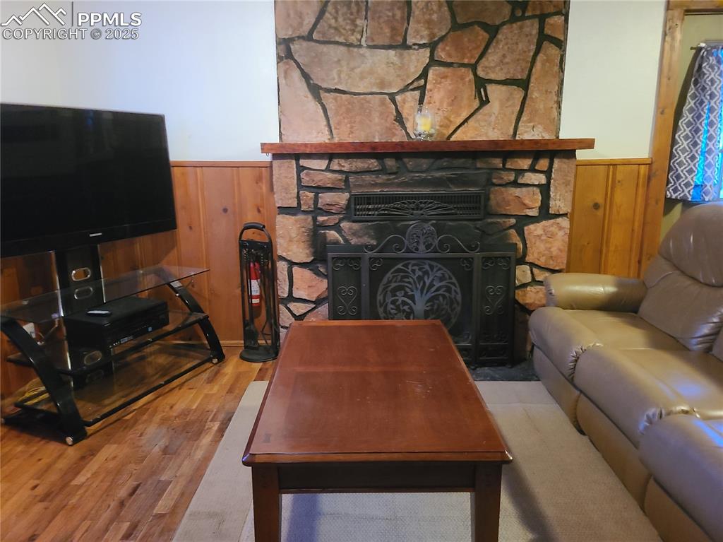 Image 17 of 20: Living room with wood walls, wainscoting, a fireplace, and wood finished fl
