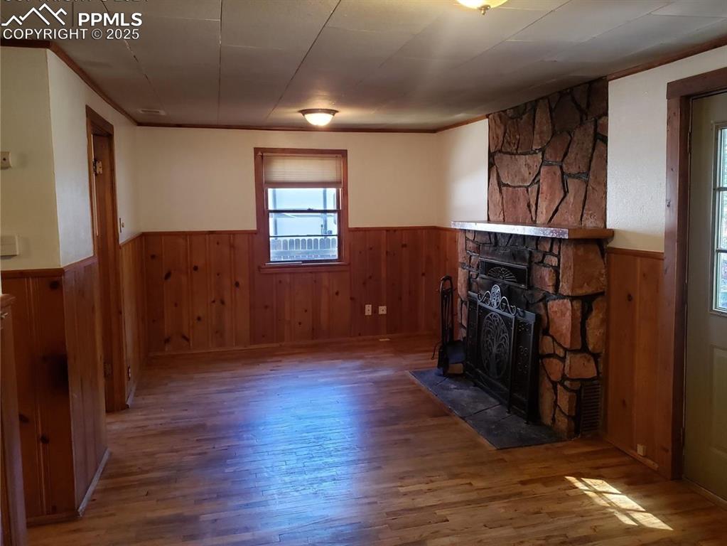 Image 7 of 20: Unfurnished living room featuring wood walls, a wainscoted wall, and wood f