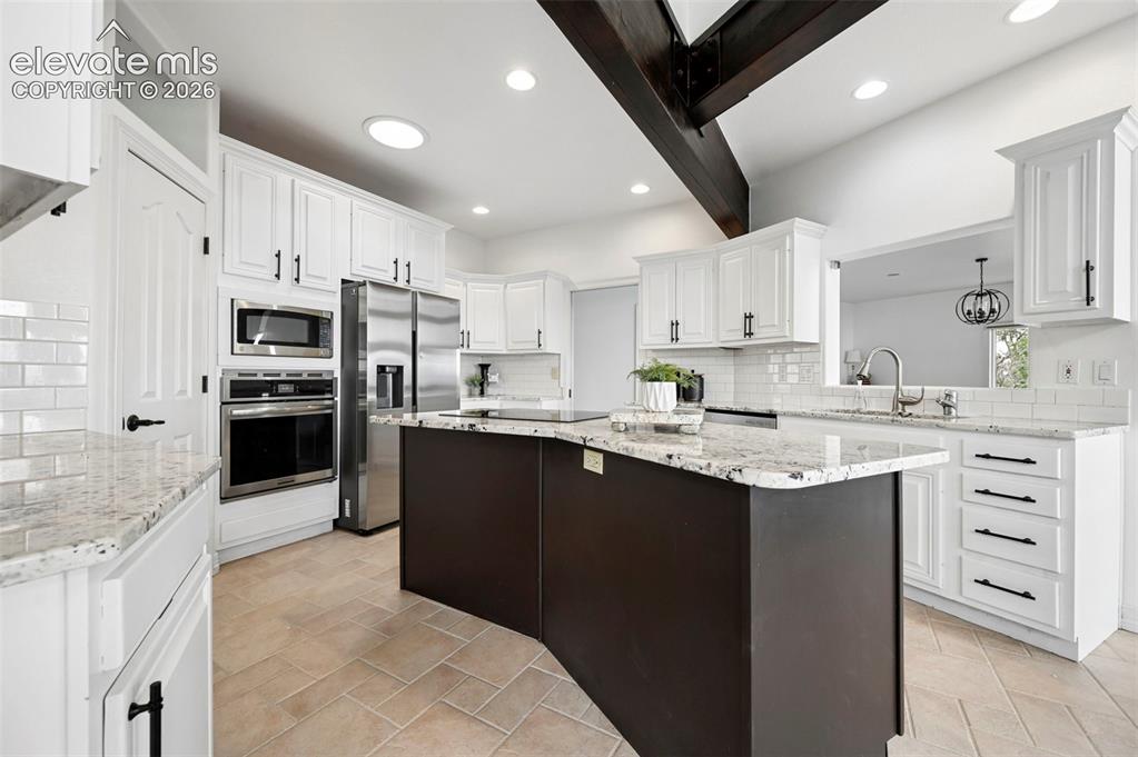 Image 13 of 45: Modern kitchen featuring a central island with a granite countertop, stainl