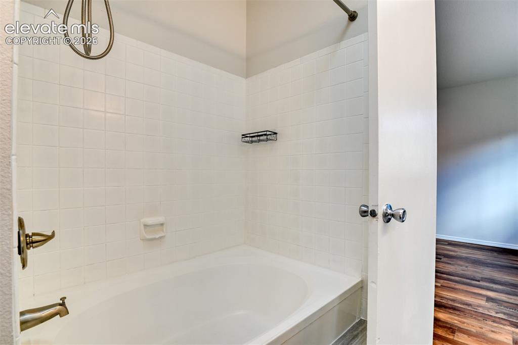 Image 24 of 48: Bathtub with white tile surround, brushed bronze fixtures, and a shower hea