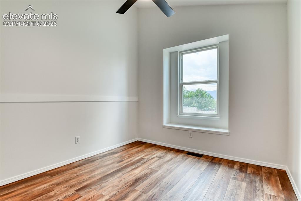 Image 28 of 48: Wood-finish flooring, white walls, single window, and ceiling fan