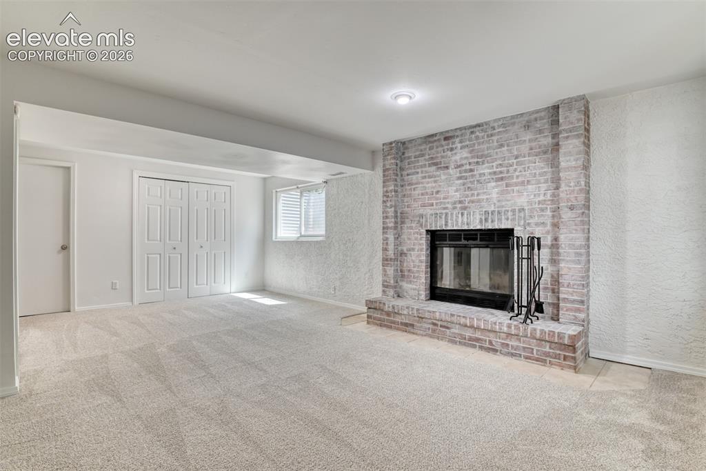 Image 38 of 48: Brick fireplace with a raised hearth, light-toned carpeting, window with ho
