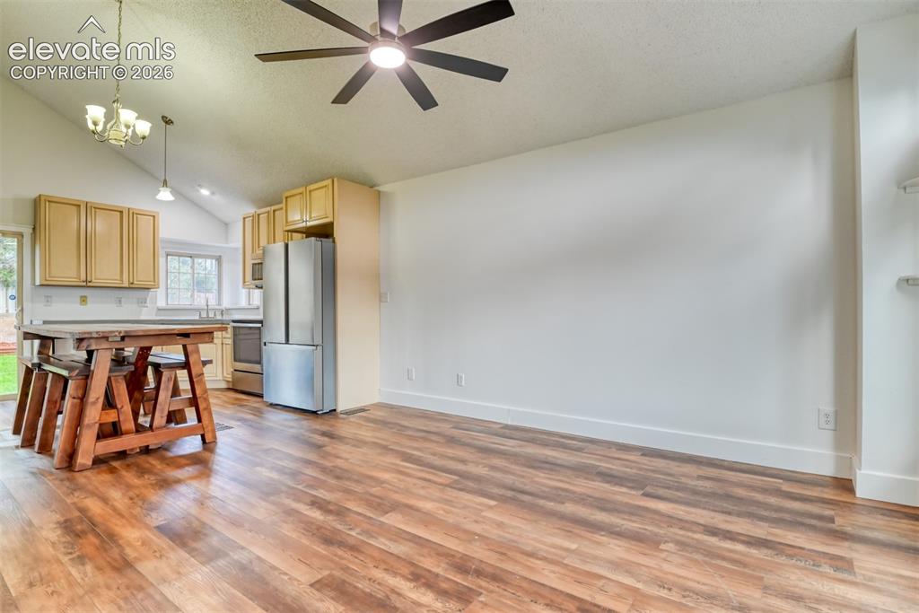 Image 8 of 48: Open-concept living area with wood-finish flooring, vaulted ceiling, and re