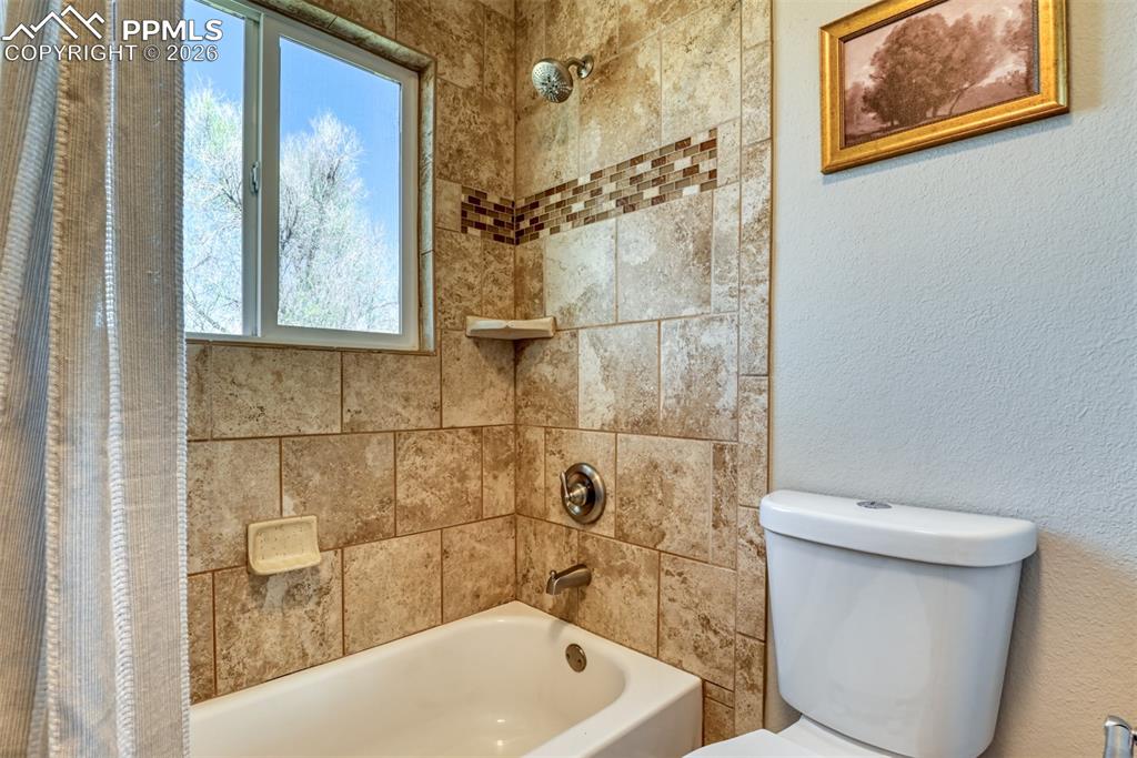 Image 21 of 39: Bathroom featuring a bathtub with a tiled surround, a showerhead, and a win