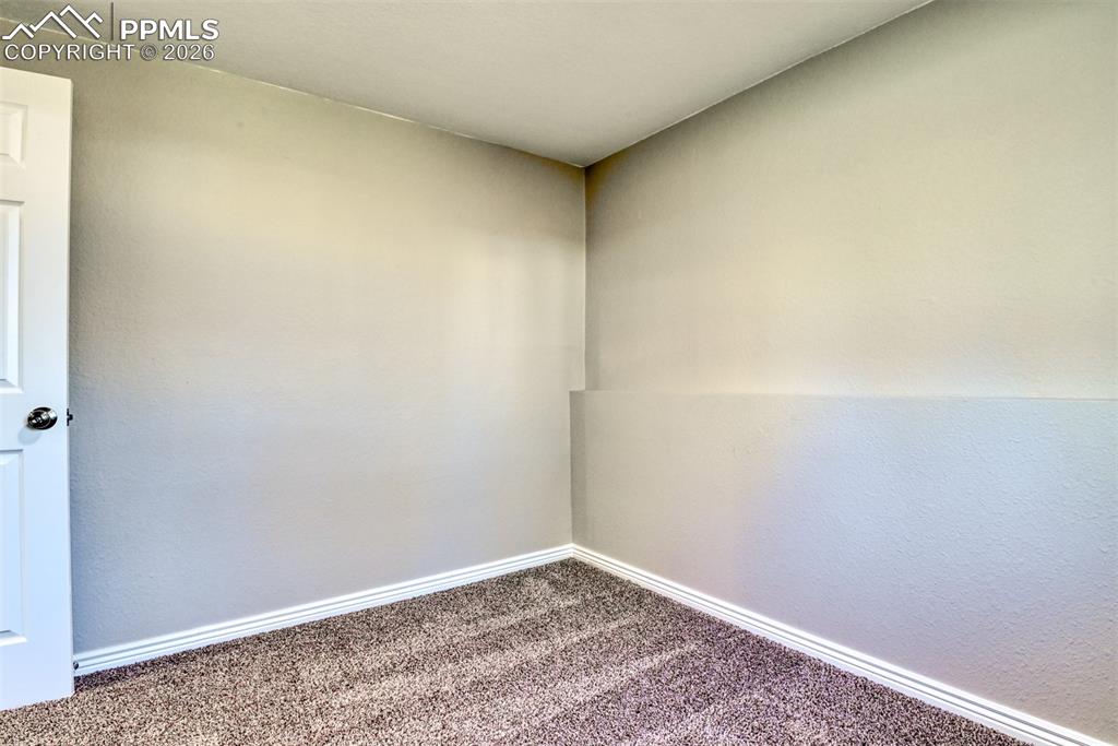 Image 35 of 39: The room features neutral-toned walls, a white door, and carpeting