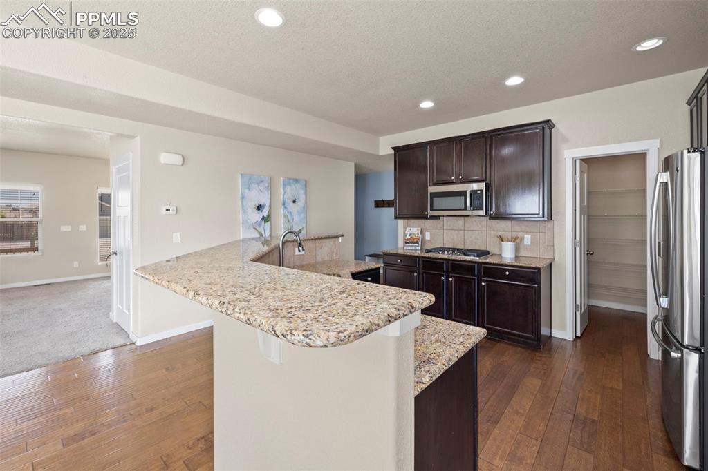 Image 12 of 31: Kitchen with stainless steel appliances, dark wood-type flooring, dark brow