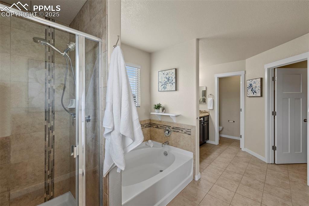 Image 19 of 31: Full bathroom with a bath, a stall shower, tile patterned floors, and a tex