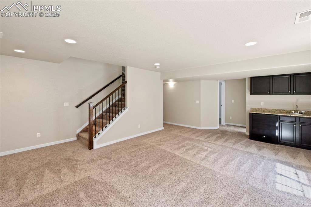 Image 27 of 31: Unfurnished living room with wet bar, light colored carpet, stairs, and rec