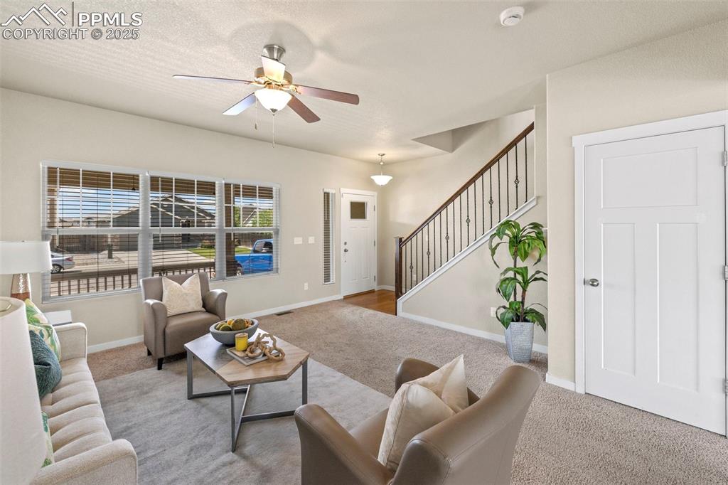 Image 8 of 31: Carpeted living area featuring ceiling fan and stairway