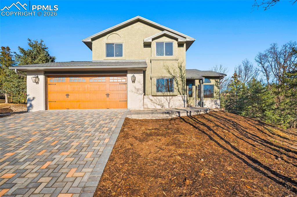 Caption: View of front of property featuring brick siding, stucco siding, decorative driveway, and garage