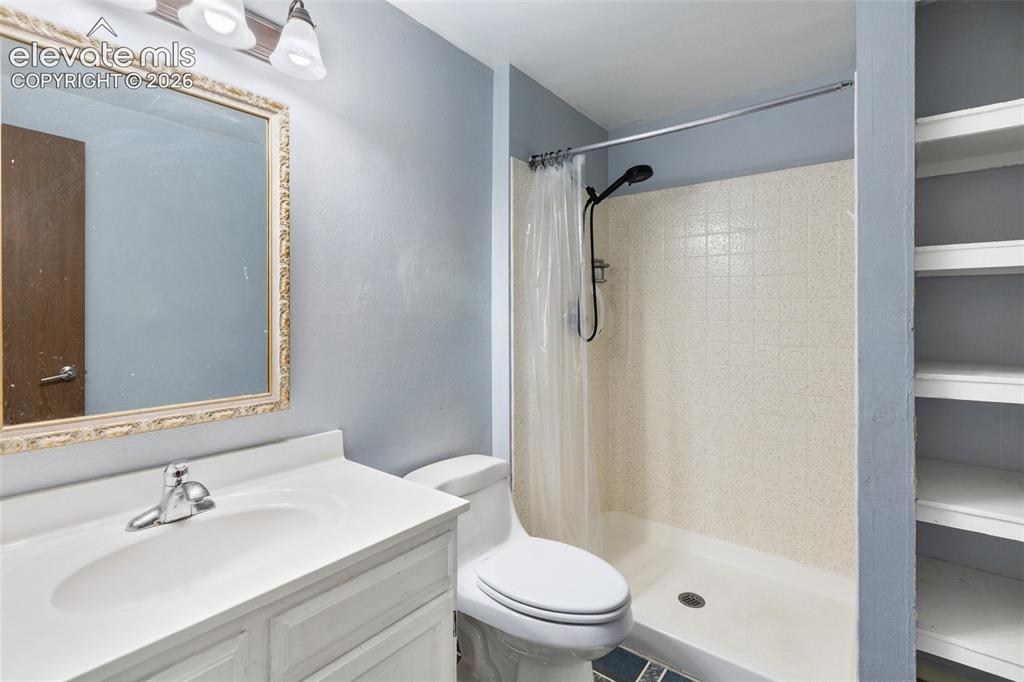 Image 15 of 27: Vanity with integrated sink, framed mirror, built-in shelving, tiled shower