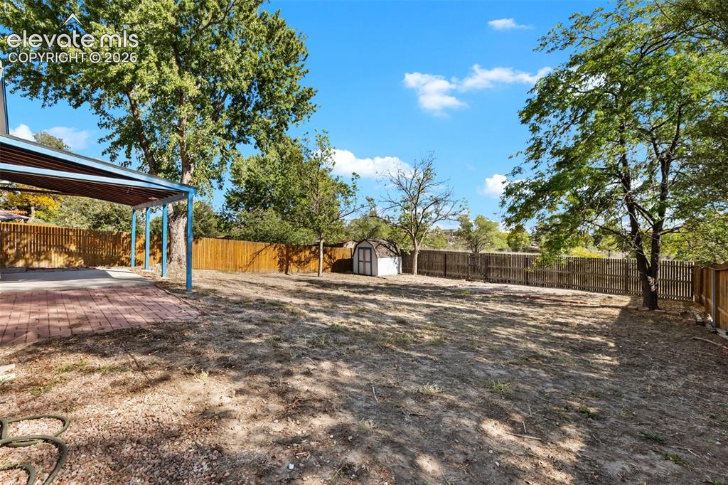 Image 19 of 27: Expansive backyard with a covered patio featuring brick pavers, a storage s