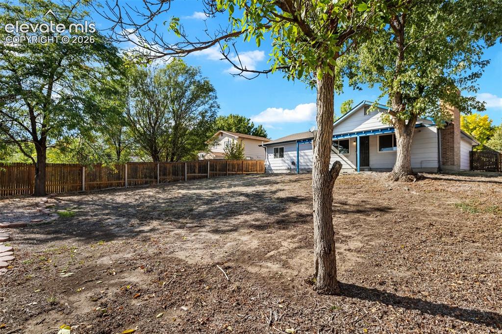 Image 20 of 27: Expansive backyard with a full privacy fence, mature trees, and a brick chi