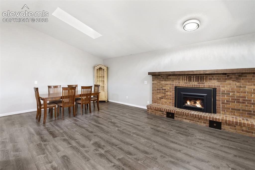 Image 23 of 27: Vaulted ceiling with skylight, wood-finish flooring, brick-clad fireplace w